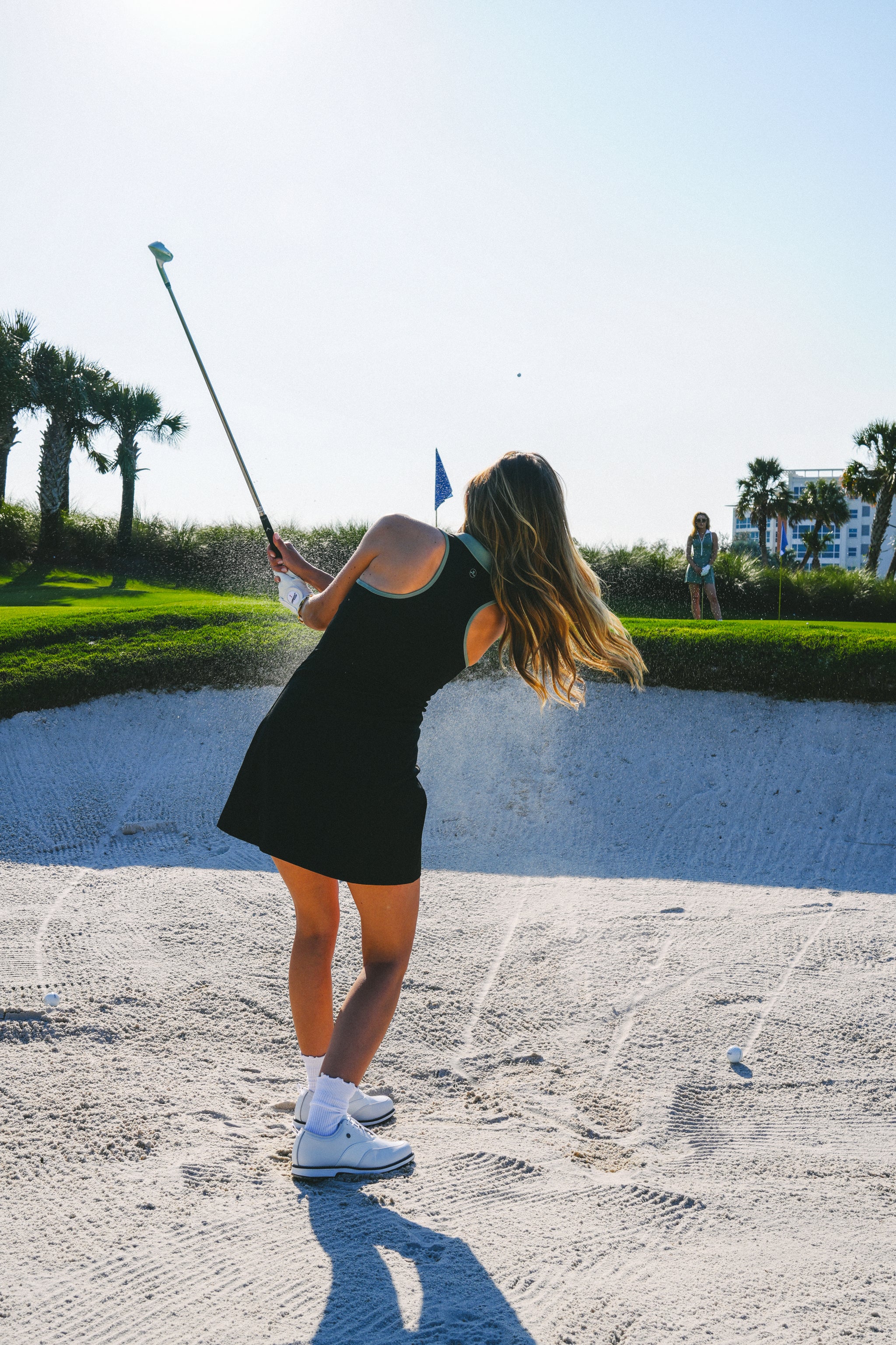 Woman playing golf on a sunny day with a green background in Maison Merritt black dress