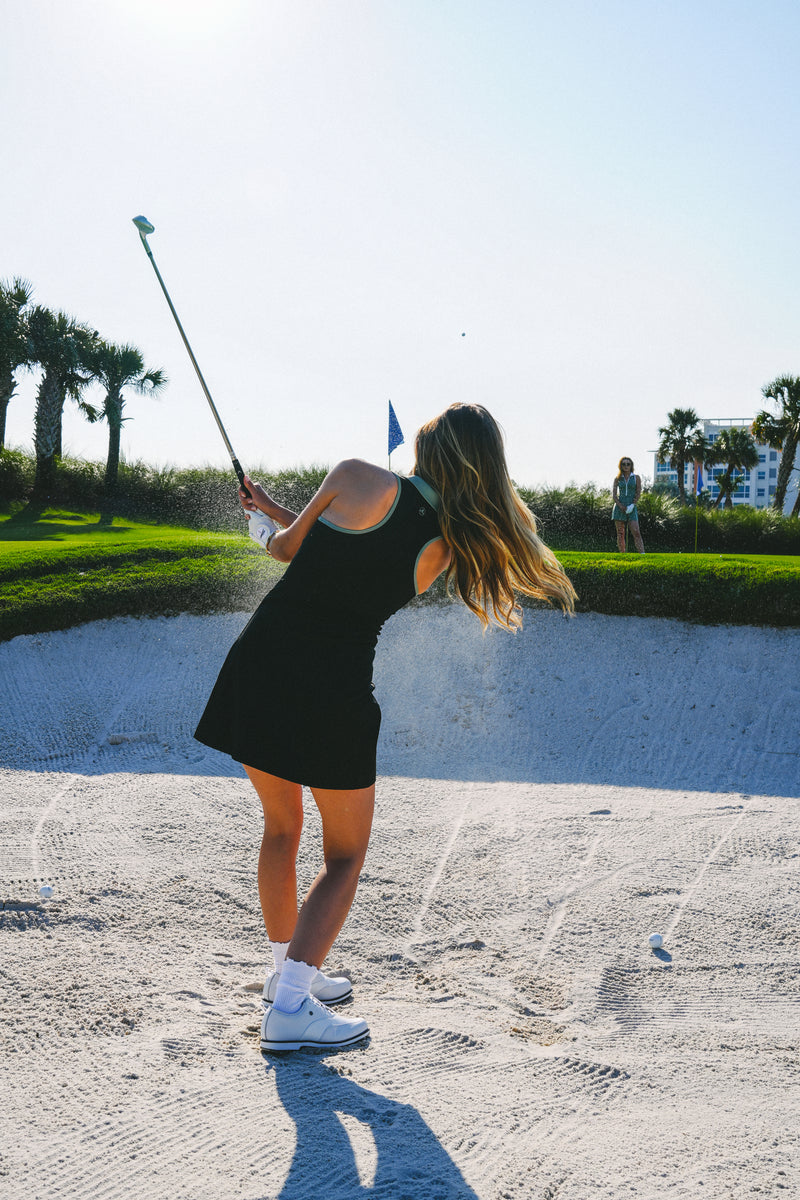Woman playing golf on a sunny day with a green background in Maison Merritt black dress
