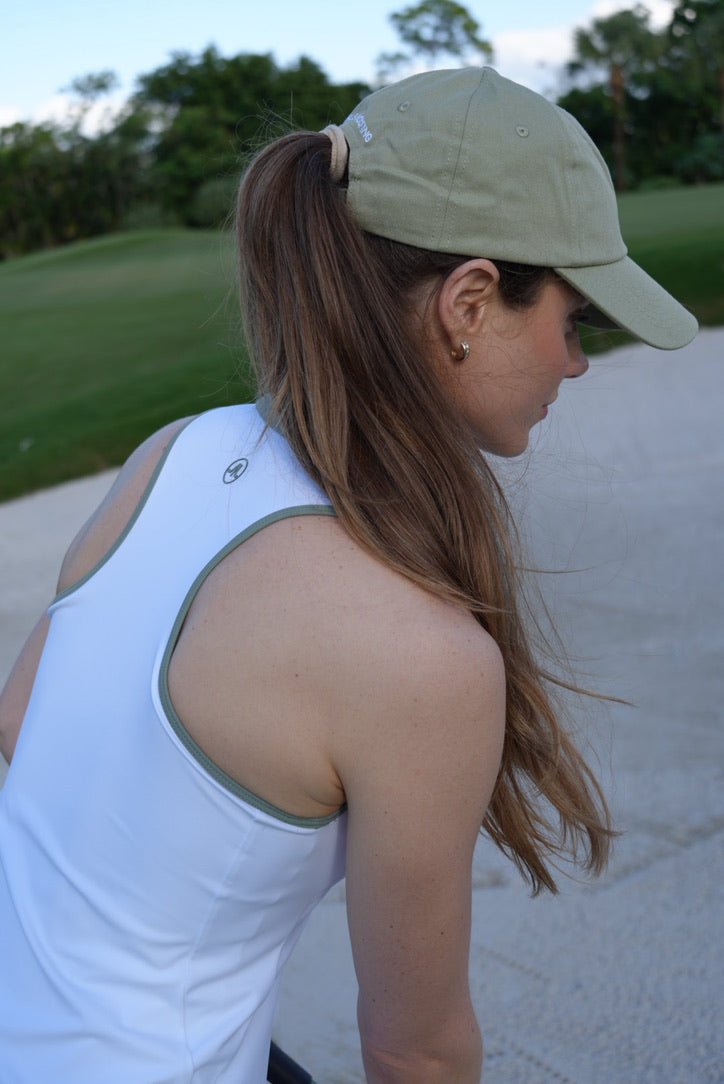 Woman in white maison merritt racerback golf dress top and green get girls golfing cap on a golf course